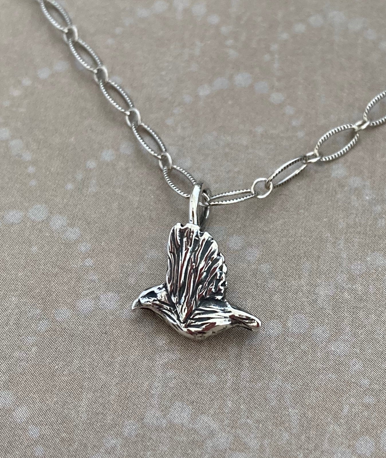 Flying Kiwikiu bird charm in silver, hanging from a chain